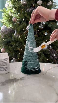 someone is decorating a small christmas tree with white paint and green yarn on it