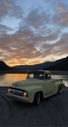 an old pick up truck parked in front of a body of water with mountains in the background