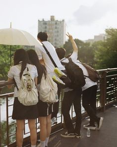 several people standing on a bridge with an umbrella over their heads and back to the camera