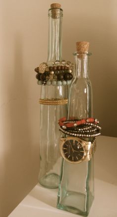 two glass bottles with bracelets and a watch on them