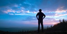 a man standing on top of a hill with his hands in his pockets as the sun sets