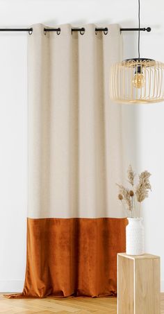 an orange and white curtain hanging in front of a wooden table with a vase on it