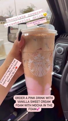 a woman holding up a pink drink in her car with stickers on the side