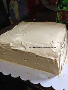 a white cake with frosting sitting on top of a table next to a bottle