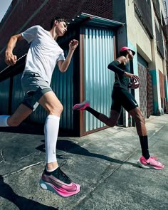 two men are running on the sidewalk in front of a building and one is wearing pink shoes