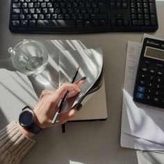 a person writing on a notepad next to a calculator and computer keyboard