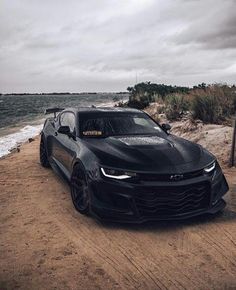 a black chevrolet camaro is parked on the beach near the water and sand dunes