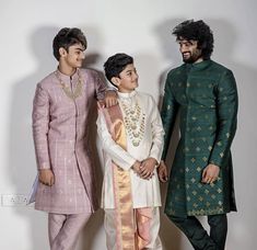 three men standing next to each other in front of a white wall wearing green and pink outfits