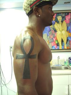 a man with an egyptian cross tattoo on his upper arm and chest, standing in front of a kitchen sink