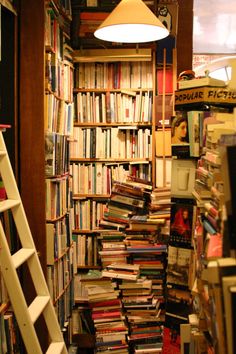 a room filled with lots of books next to a ladder and light above the book shelf