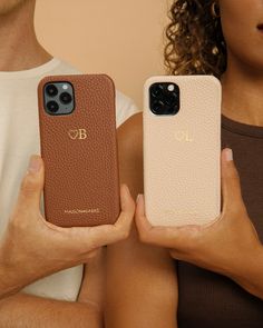 two people holding up their cell phones in front of them, one is brown and the other is beige