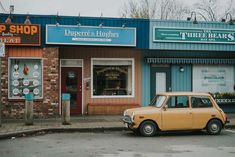 an old yellow car is parked in front of a store with signs on the windows