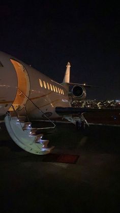 an airplane sitting on the tarmac at night with stairs leading up to it's door