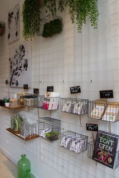 several shelves with books and plants hanging on the wall in a room that has white tiled walls