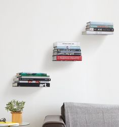 three books are stacked on the wall near a couch and table with a plant in it