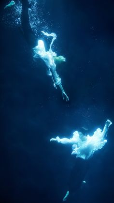 two people floating in the water with their arms spread out and feet up above them