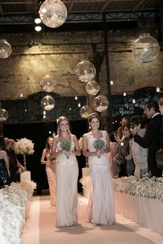 two bridesmaids walking down the aisle with bubbles in the air above them and onlookers