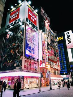 people are walking around in front of a building with many advertisements on it at night