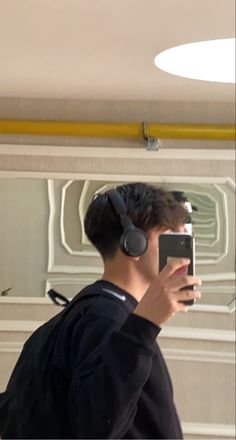 a man wearing headphones is taking a selfie in front of a mirror with his cell phone