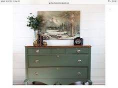 an old dresser painted green and has a painting on the wall above it with a clock