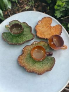 three tea cups and saucers sitting on top of a leaf shaped plate in the grass