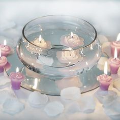 several candles are floating in a bowl with water and petals on the tablecloth,