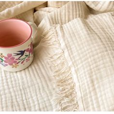 a coffee cup sitting on top of a bed covered in white sheets and blankets with pink flowers