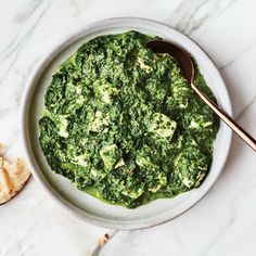 a white bowl filled with spinach and bread on top of a marble countertop