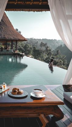 a table with food on it in front of a pool and some people sitting at the edge