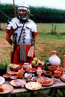 a man dressed in roman armor standing next to a table full of food