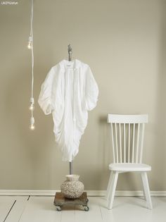 a white chair sitting next to a white shirt on a hanger in a room