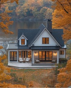 a white house sitting on top of a lush green hillside next to a lake in the fall