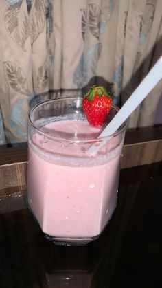 a strawberry sitting on top of a glass filled with liquid and a straw in it