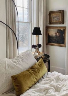 a bed with white sheets and pillows in front of a painting on the wall next to a window