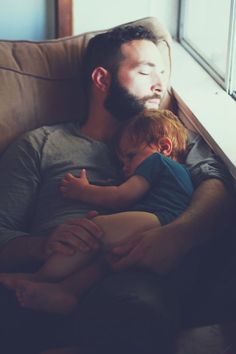 a man laying on top of a brown couch next to a little boy with his eyes closed