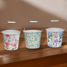 three buckets sitting on top of a wooden table with flowers painted on the sides