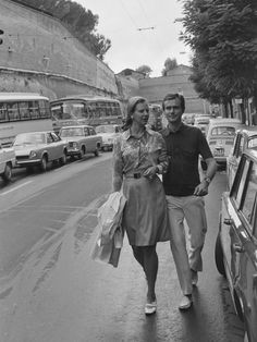 a man and woman walking down the street in front of cars on a rainy day