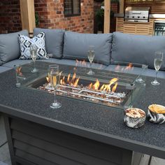 a fire pit sitting on top of a table next to two wine glasses and food