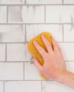 a hand holding a sponge on top of a white brick wall with grouting