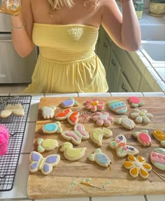 a woman in a yellow dress is holding a glass and looking at some decorated cookies