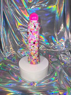 a pink and purple object sitting on top of a white pedestal in front of a metallic backdrop