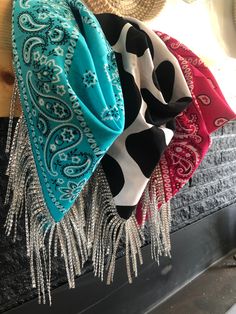 three different colored scarves hanging on a wall next to a fireplace with silver chains