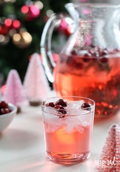 cranberry tea in a glass mug next to a pitcher and small christmas trees