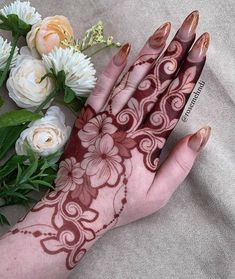 a woman's hand with henna on it next to flowers