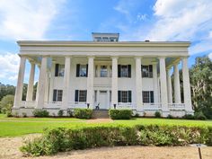 a large white house with columns and pillars on the front porch is surrounded by greenery