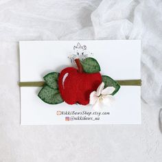 a red apple with green leaves and a white flower on it's headband