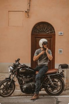 a man sitting on top of a motorcycle next to a brown building and wearing a helmet