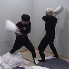 two young men in black shirts and pants are playing with white sheets on the floor