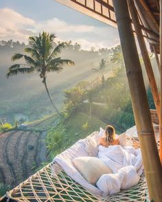 a woman laying in a hammock on top of a lush green hillside with palm trees