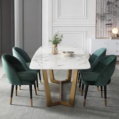 a marble dining table with green chairs and a vase on the end, in front of a white paneled wall